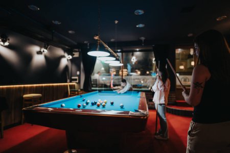 A group of friends engage in a fun-filled game of pool at a cozy, dimly lit billiards room, expressing carefree recreation and camaraderie.