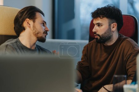 An intimate and focused shot of two men having a serious discussion indoors. Natural light bathes the scene, highlighting the genuine expressions and engagement between them.