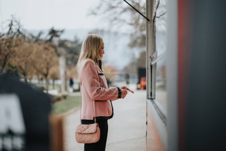 Una mujer profesional en un abrigo rosa espera el café del camión de café, mientras se va a casa después del trabajo.