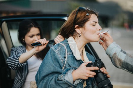 Zwei Freundinnen genießen die gemeinsame Zeit im Freien, die eine zündet sich eine Zigarette für die andere an, die eine Spiegelreflexkamera in der Hand hält und aufrichtige urbane Momente einfängt.