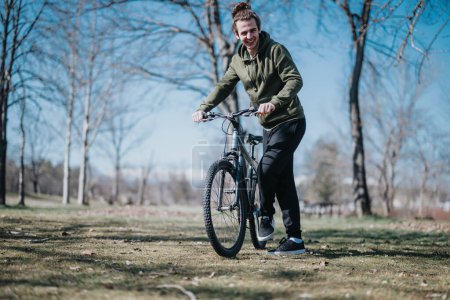 Dans cette image vibrante, un beau jeune homme sourit tout en faisant du vélo à l'extérieur dans un parc, capturant parfaitement un moment de loisirs et de plaisir par une journée ensoleillée.
