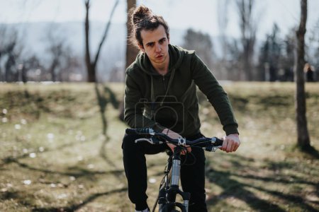 A young man pauses during a bike ride to relax and enjoy the serene atmosphere of a sunlit park. Perfect for portraying outdoor leisure and fitness.