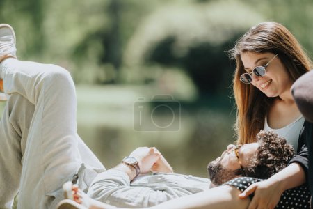 Carefree young couple lounging in a park, reveling in the sun with smiles. Casual clothing enhances their comfortable, joyful weekend outdoor.