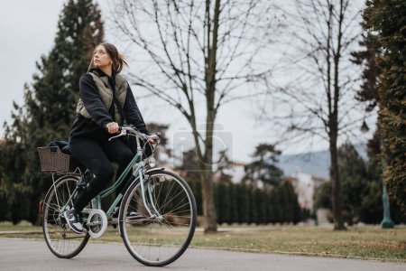 A contemplative young woman pedals leisurely on her bicycle through a serene park, with trees and a tranquil ambiance surrounding her.