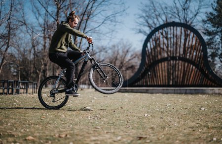 A young adult male cycles confidently in a vibrant park, showcasing dynamic motion and a scenic backdrop with an iconic bridge.