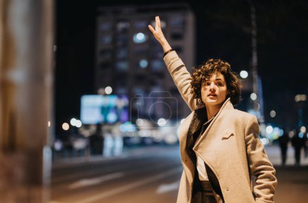 Young woman hailing a cab on a bustling city street at night.