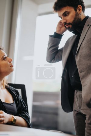 Una conversación profesional se intensifica a medida que un trabajador masculino expresa su preocupación mientras una colega escucha atentamente en un entorno de oficina bien iluminado.