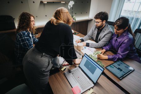 Eine Gruppe unterschiedlicher Fachleute arbeitet aktiv an einem Tisch in einem Büroumfeld und diskutiert Dokumente und digitale Daten..