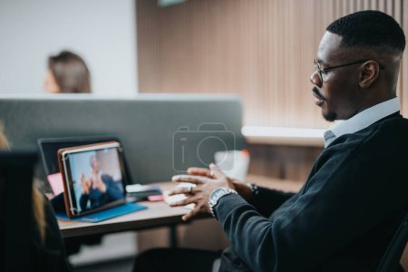 A professional African American businessman engages actively in a team discussion while sitting in a well-equipped office, demonstrating effective teamwork and communication.