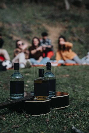 Group of friends relaxing on a picnic blanket in the park with bottles of drink and a guitar, sharing a jovial moment.