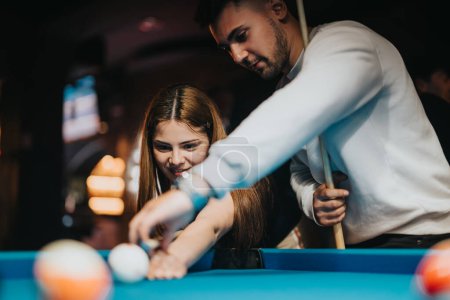A man and woman share a playful moment while playing pool, surrounded by the warm ambiance of a billiard hall.