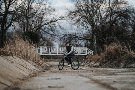 A teenage boy cycles down a tranquil park pathway, embracing freedom and nature on his bicycle.