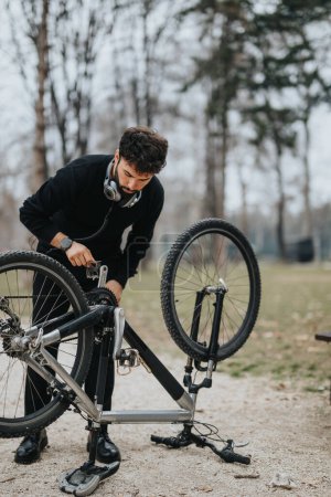 Hombre de negocios enfocado en atuendo casual reparando una bicicleta de montaña al aire libre, mostrando multitarea y equilibrio entre vida laboral y personal.