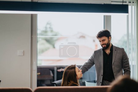 A charming male worker engaging with a female colleague in a warmly lit, modern office, conveying a casual business interaction.