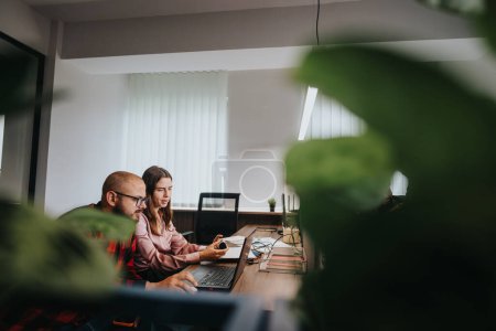 Zwei Geschäftskollegen, ein Mann und eine Frau, arbeiten gemeinsam an einem Laptop in einem gut beleuchteten Büro. Teamwork und Produktivität im Unternehmensumfeld stehen im Fokus.