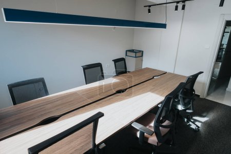 Dieses Bild zeigt einen modernen Büro-Konferenzraum mit einem langen Holztisch und stilvollen modernen Stühlen in einem sauberen und minimalistischen Interieur..