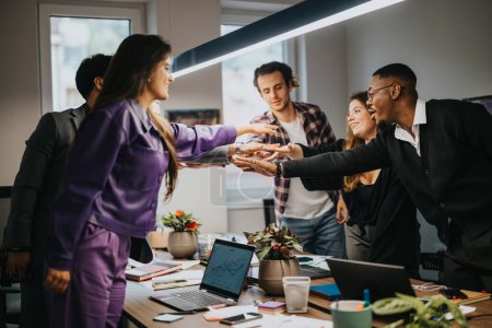 A team of diverse coworkers celebrate a successful project in their office with enthusiasm and teamwork, showing collaboration and achievement.