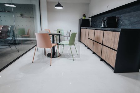 Moderner Büroraum mit lebhaften grünen und pfirsichfarbenen Stühlen, einer stilvollen Küchenzeile und einem gläsernen Besprechungsraum.