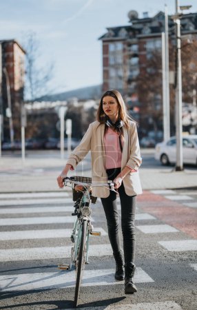 Fashionable young woman walking with her bike across the zebra crossing in an urban setting, reflecting an eco-friendly lifestyle.