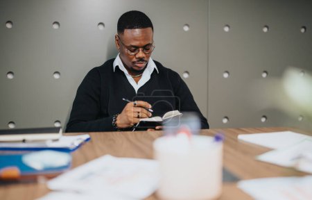 Un hombre de negocios profesional es representado escribiendo intensamente en un cuaderno en su escritorio de oficina, rodeado de carpetas y suministros de oficina, encarnando la concentración y dedicación a su trabajo.