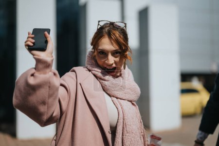 Joyful business associate in a pink coat with her phone on a bright sunny day in a modern urban setting.