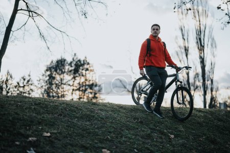 Ein lässiger junger Mann steht mit seinem Fahrrad in der Freizeit im Stadtpark und steht für einen gesundheitsbewussten Lebensstil..