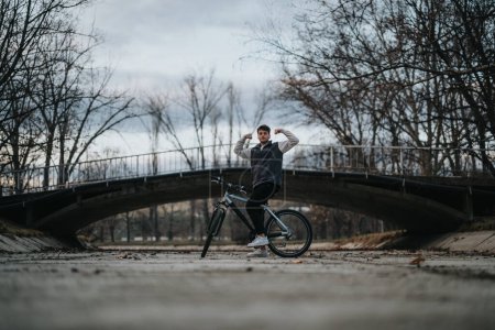 A young teenage boy pauses for a break on his bicycle under a picturesque bridge, relishing his leisure time outside.