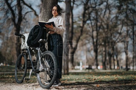 A young girl enjoys her weekend with a book, leaning on her bicycle in a sunlit park setting.