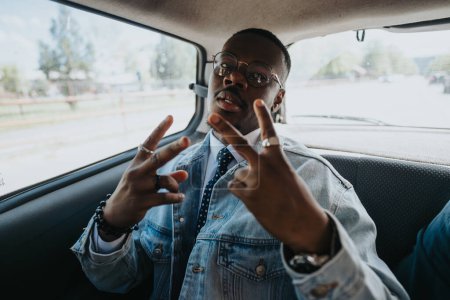 Ein trendiger junger schwarzer Geschäftsmann, der in Jeansjacke und Krawatte auf der Rückbank eines Autos sitzt und Friedenszeichen blinkt.
