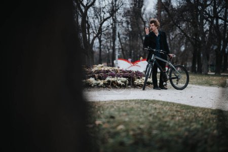 A young business person stands with a bicycle in an urban park, actively engaged in a remote work call on their smart phone.