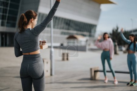 Woman in fitness attire greeting friends in urban setting, showcasing active lifestyle and friendship.