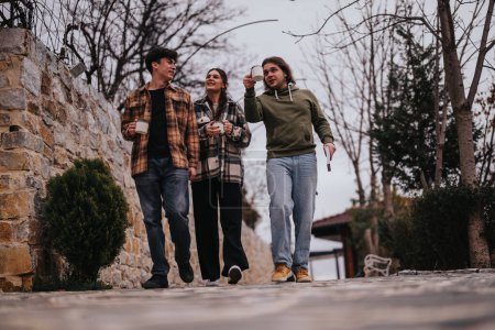 Trois amis joyeux marchent côte à côte à l'extérieur, partageant des histoires avec un café à la main, incarnant l'amitié et les loisirs.