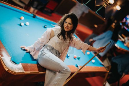 A joyful young woman plays pool at a vibrant bar, reflecting a night out filled with fun and games among friends.