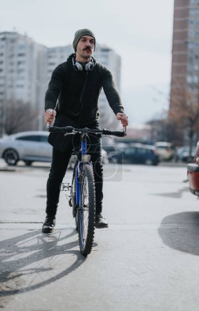 Un cycliste urbain masculin fait du vélo dans une rue de la ville avec des écouteurs autour du cou, profitant d'une journée ensoleillée à l'extérieur.