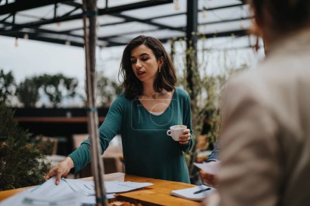 Professionelle Frau in lässiger Kleidung hält eine Kaffeetasse in der Hand, während sie sich mit einem Mitarbeiter draußen an einem Geschäftstreffen beteiligt.