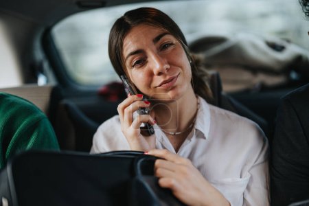 A professional woman making a phone call with a thoughtful expression, riding in the backseat of a car.