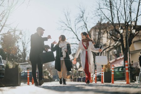 A group of fashionably dressed friends enjoying a conversation while walking along a sunny, urban street lined with trees.