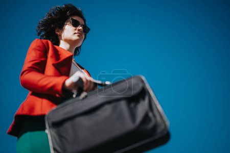 Professional businesswoman in a red blazer carrying a briefcase under the clear blue sky signifies ambition and determination.