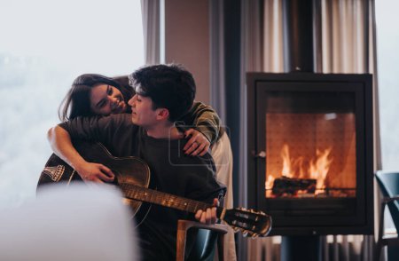 Un moment chaleureux comme un couple profite du temps à la maison avec une guitare près d'une cheminée chaude et flamboyante.