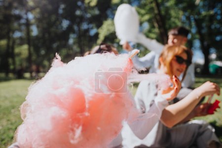 A group of friends sit outdoors in a park, sharing smiles and cotton candy on a bright sunny day, embodying joyful leisure moments.
