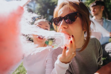 Group of friends sharing cotton candy outdoors on a bright, sunny day, embodying happiness and leisure in a green park setting.