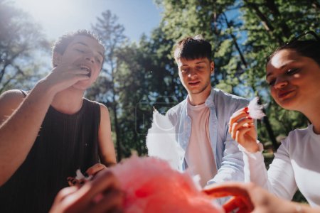 Three young adults share candy floss and enjoy a sunny day together in the park, embodying joy and youthful freedom.