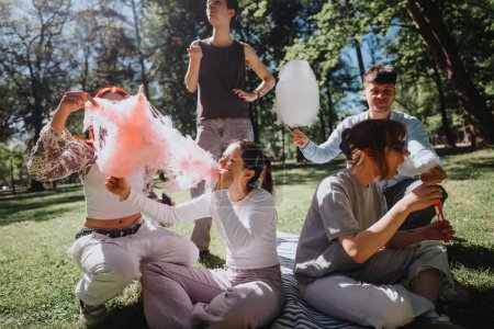 Ein fröhliches Treffen von Freunden, die an einem sonnigen Tag im Park Zuckerwatte essen, um Glück und Freizeit im Freien zu präsentieren.
