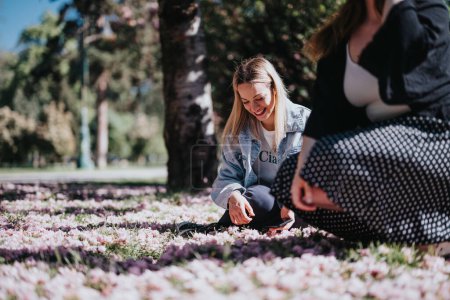L'image capture une scène joyeuse de deux amis dans un parc, l'un cueillant des fleurs de cerisier tandis que l'autre regarde avec appréciation.
