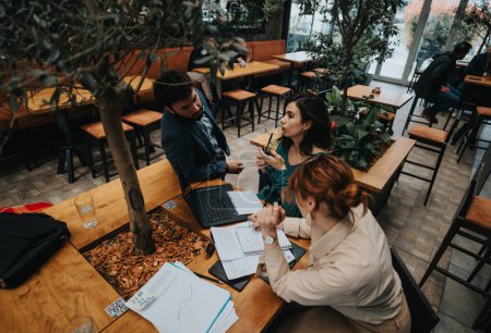 Se ve a un equipo dinámico de startups discutiendo estrategias de negocio sobre el café en una cafetería urbana moderna.