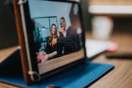 L'image montre deux collègues d'affaires engagés dans une poignée de main virtuelle à travers une tablette, reflétant un environnement de travail à distance convivial et professionnel.