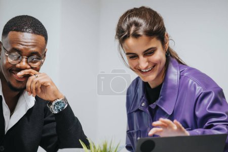 Ein junger Mann und eine junge Frau, professionell gekleidet, teilen einen freudigen Moment während eines produktiven Geschäftstreffens, während sie Wachstumsstatistiken auf einem Laptop in ihrem Büro überprüfen..