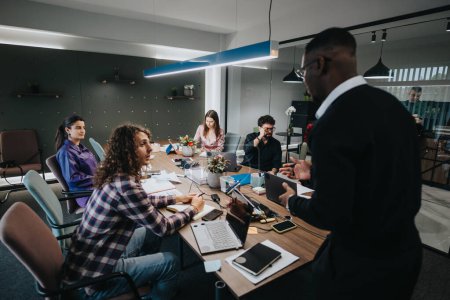 Ein multikulturelles Team von Mitarbeitern diskutiert Strategie und Zusammenarbeit an einem Konferenztisch in einem hell erleuchteten modernen Büro. Fokus auf Teamwork und kreative Problemlösung.