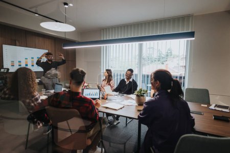 A mixed race group of young entrepreneurs collaborates in a well-lit office meeting room, focusing on presentation charts and business growth.