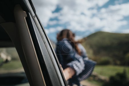 Una joven con un vestido a rayas se asoma por la ventana de un coche, sintiendo la brisa, con un paisaje borroso en el fondo.